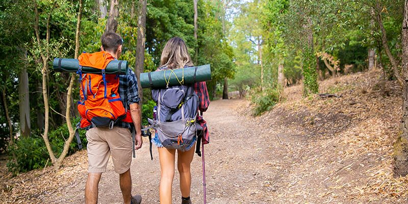 back-view-couple-going-along-road-forest-long-haired-woman-man-carrying-backpacks-hiking-nature-together-green-trees-background-tourism-adventure-summer-vacation-concept copia