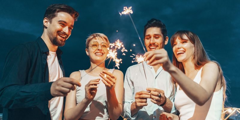 Friends enjoying a rooftop party and dancing with sparklers in hands
